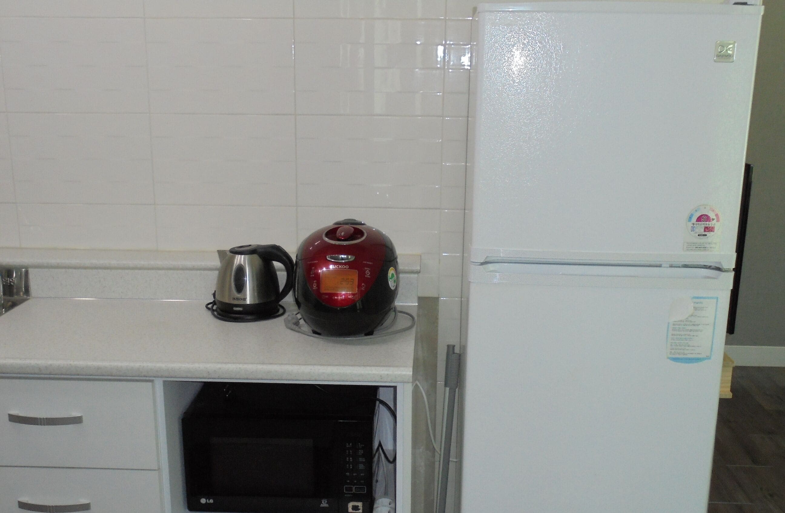 A kitchen with a microwave, a kettle, and a refrigerator.