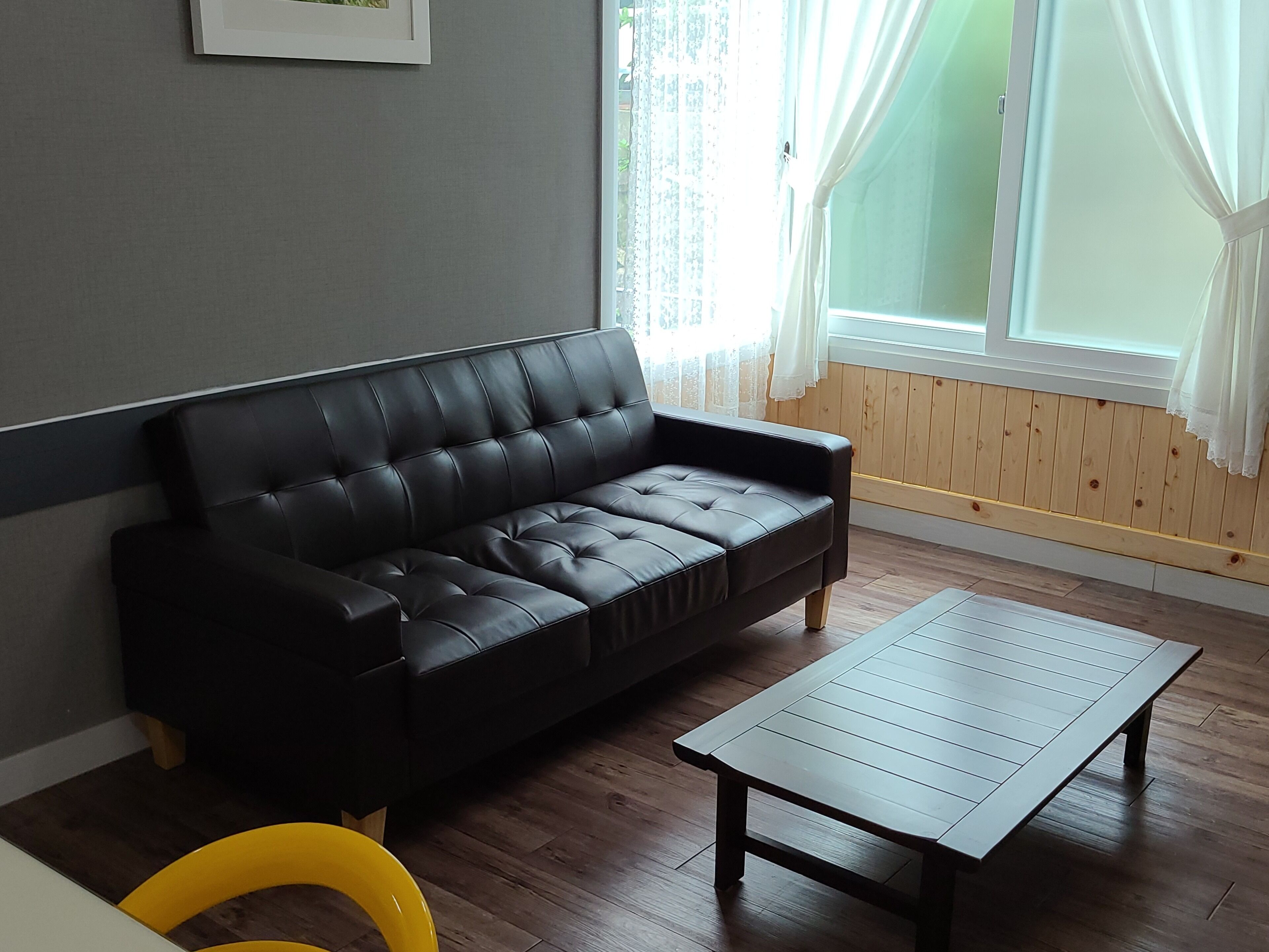 A modern living room with a black leather sofa, a wooden coffee table, and a yellow chair.
