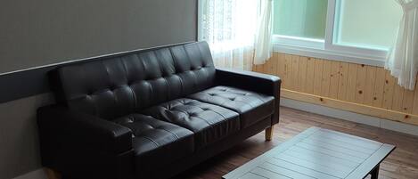 A modern living room with a black leather sofa, a wooden coffee table, and a yellow chair.