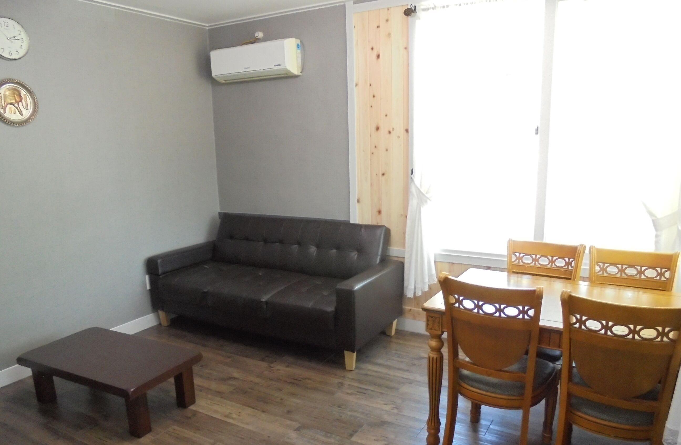 A living room with a dark leather sofa, a wooden coffee table, and a dining table with wooden chairs.