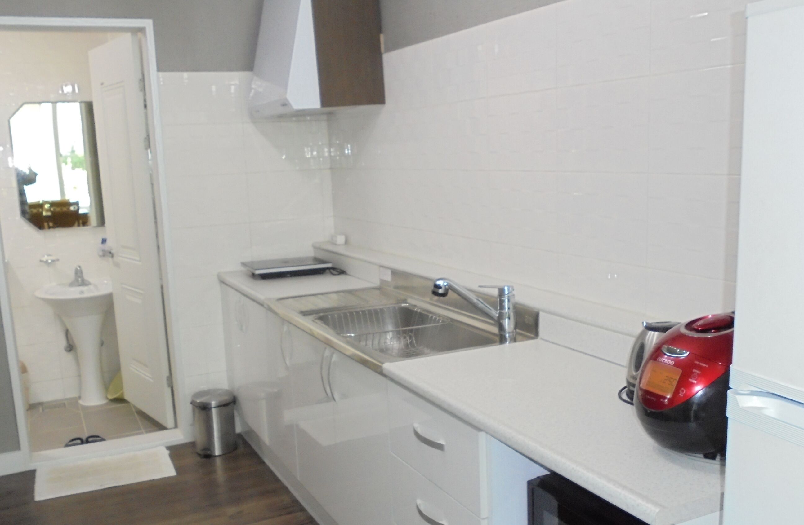 Una cocina moderna con armarios blancos, un fregadero de acero inoxidable y una cafetera roja.