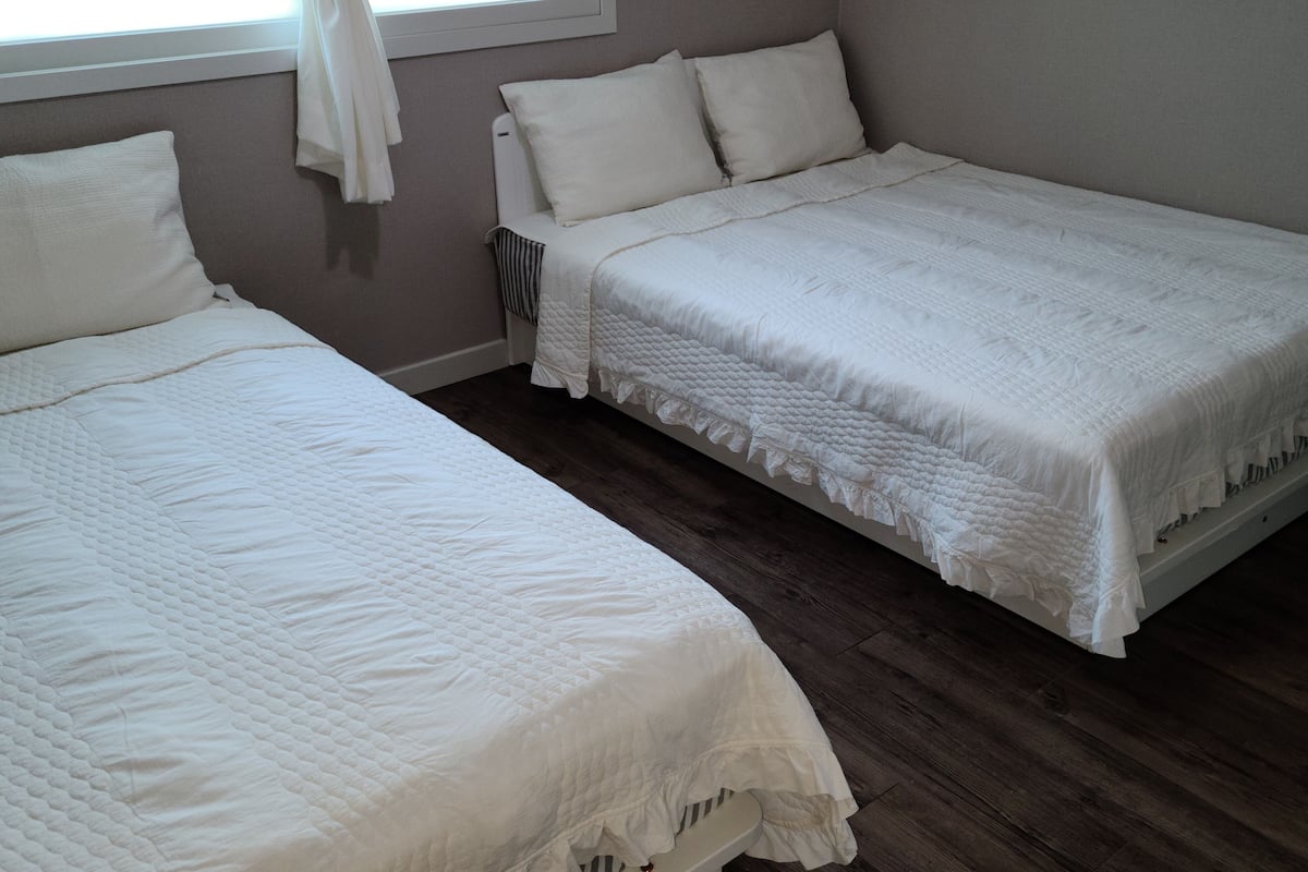 Two single beds with white bedding in a room with wooden flooring and a window with curtains.