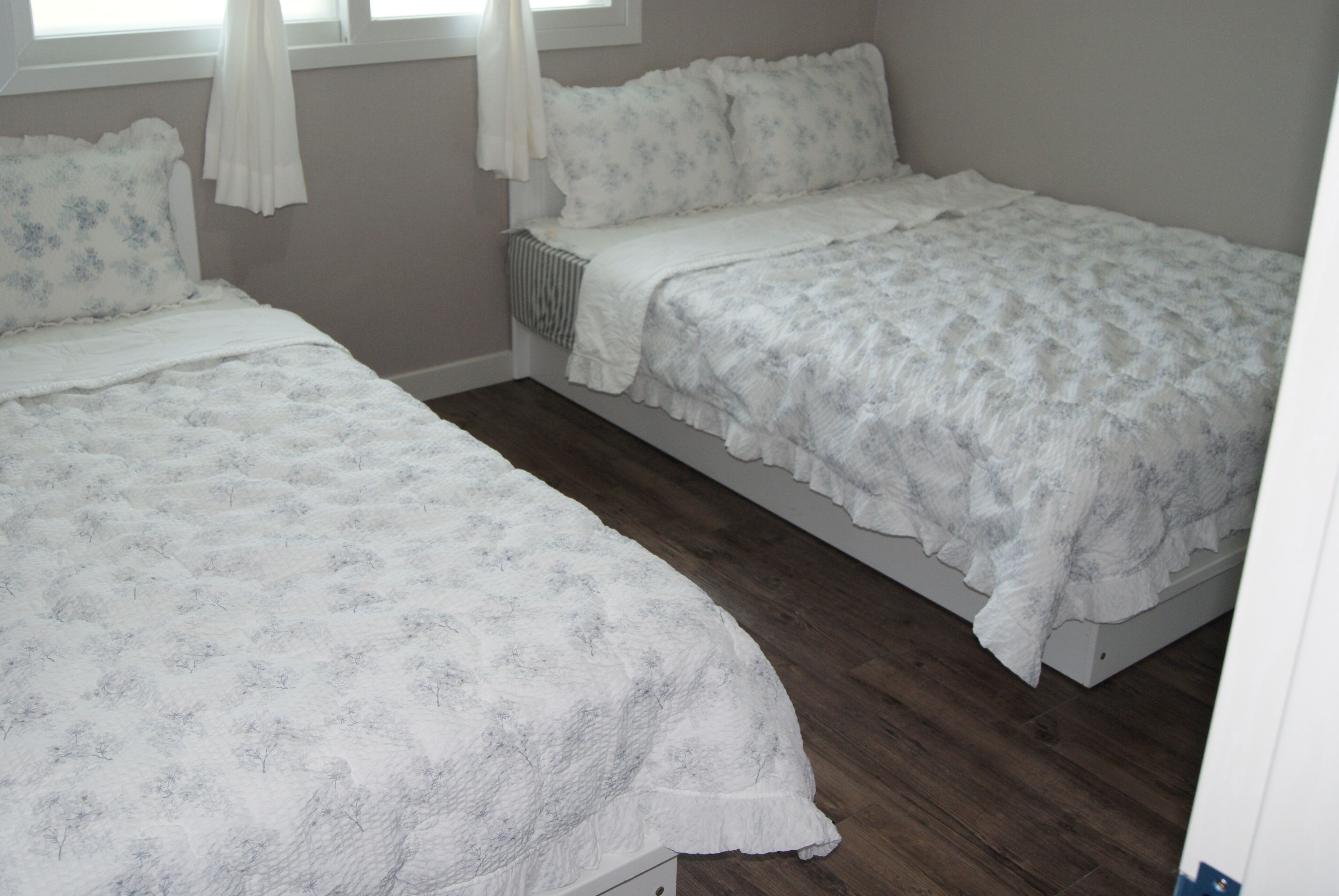 A bedroom with two single beds, a radiator, and a window with curtains.