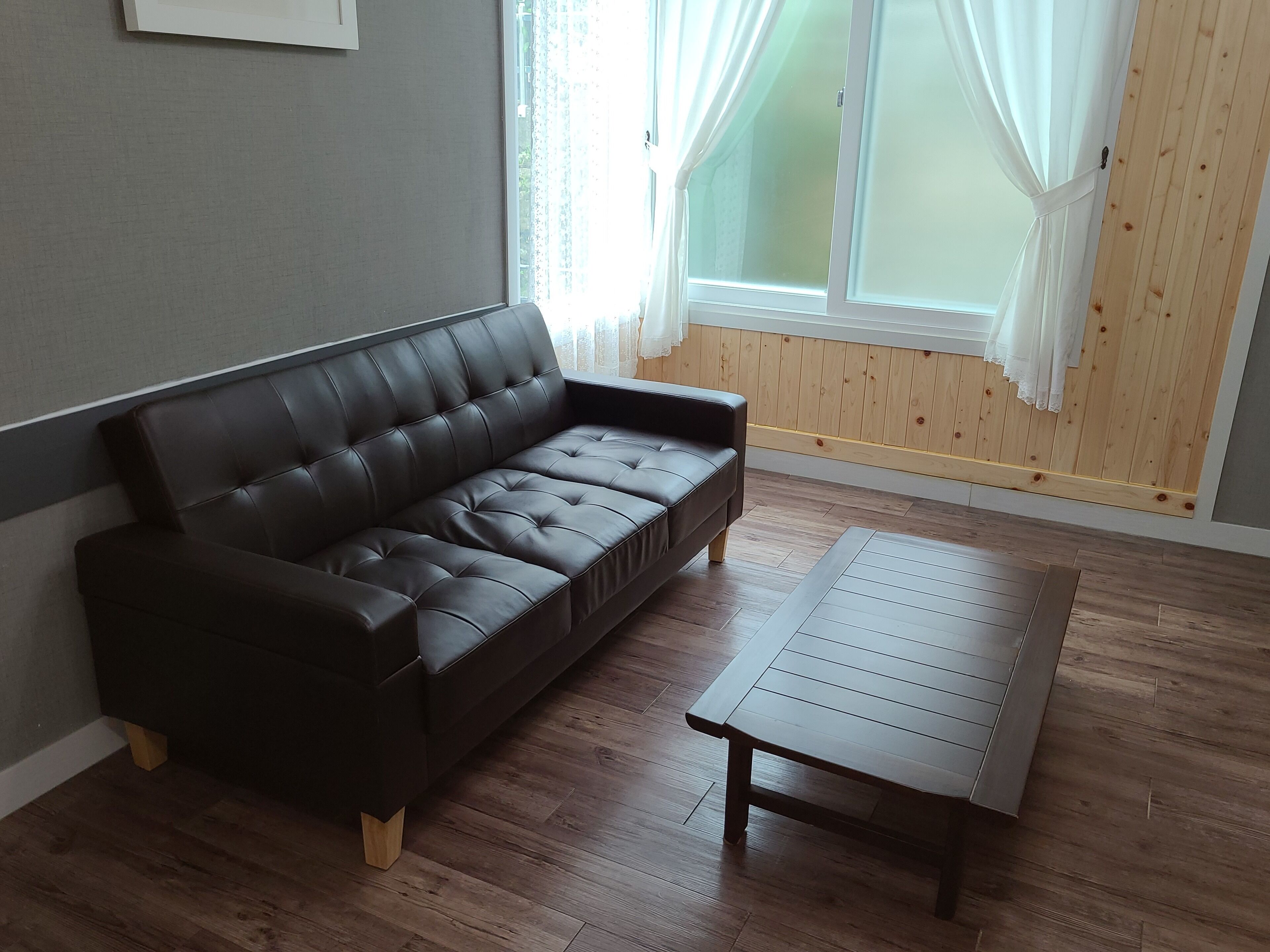 Uma sala de estar moderna com um sofá de couro escuro, uma mesa de centro de madeira e uma grande janela com cortinas leves.