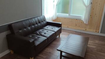 Uma sala de estar moderna com um sofá de couro escuro, uma mesa de centro de madeira e uma grande janela com cortinas leves.