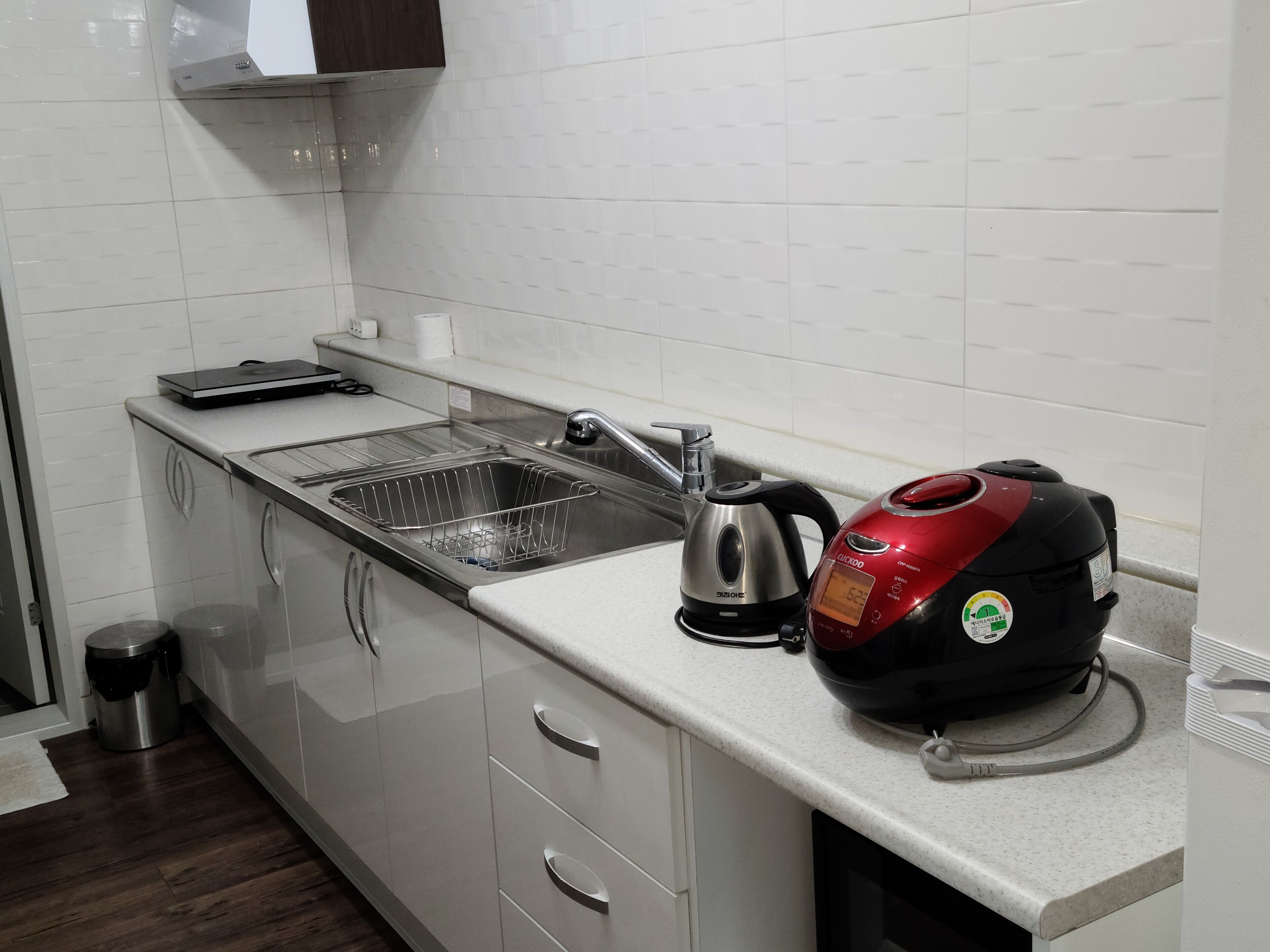 A kitchen with a stainless steel sink, a kettle, and a red electric kettle on the countertop.