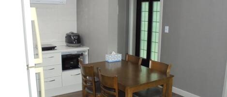 Un comedor con una mesa y sillas de madera, una pequeña cocina con refrigerador y microondas, y un ventanal con vidrio tintado de verde.