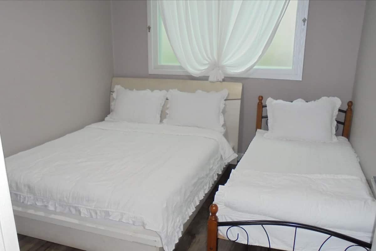 Two single beds with white bedding, a window with white curtains, and a wooden headboard.