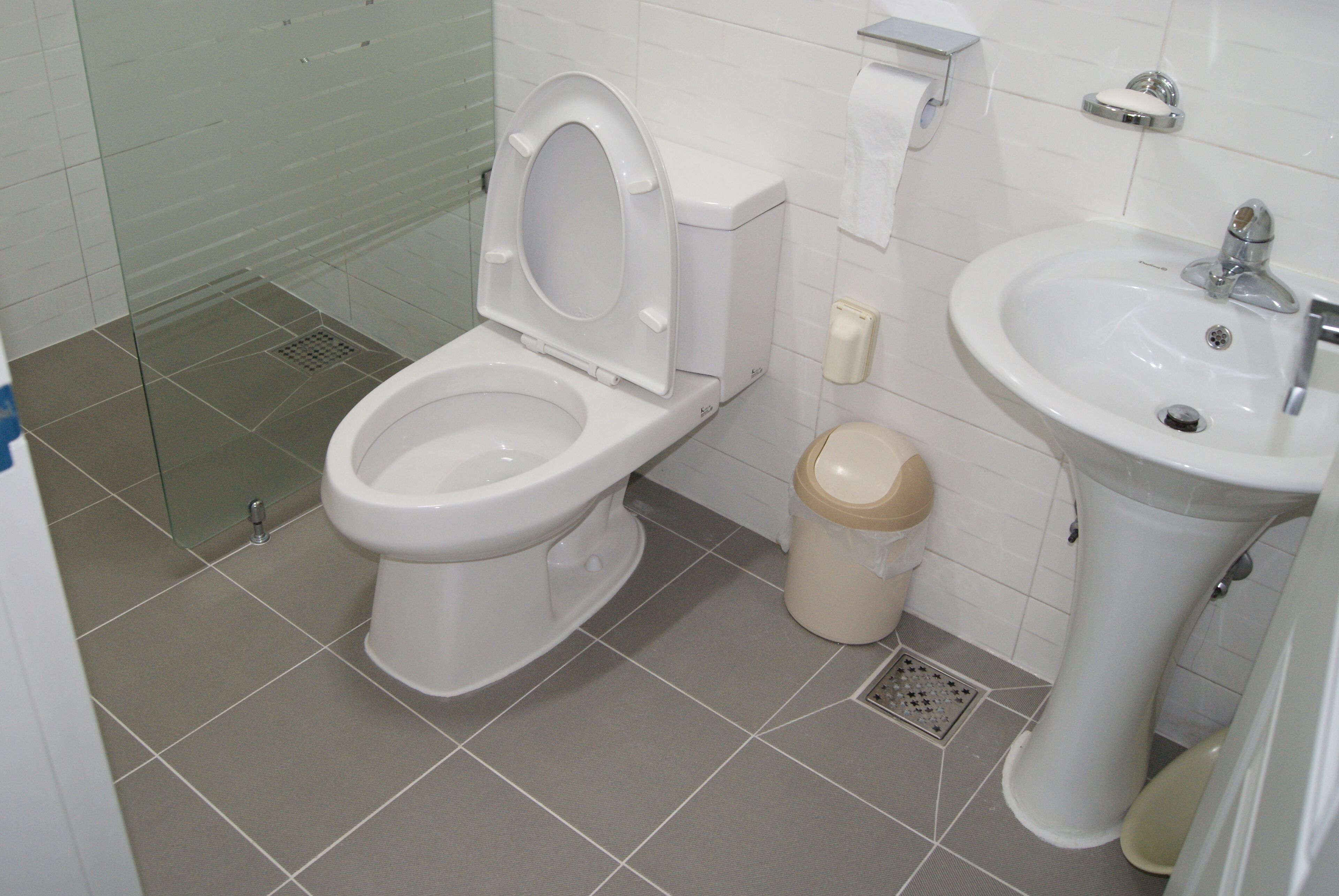 A bathroom with a toilet, bidet, sink, and a trash bin.