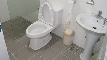 A bathroom with a toilet, bidet, sink, and a trash bin.