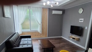 A living room with a sofa, a coffee table, a TV, and a window with curtains.