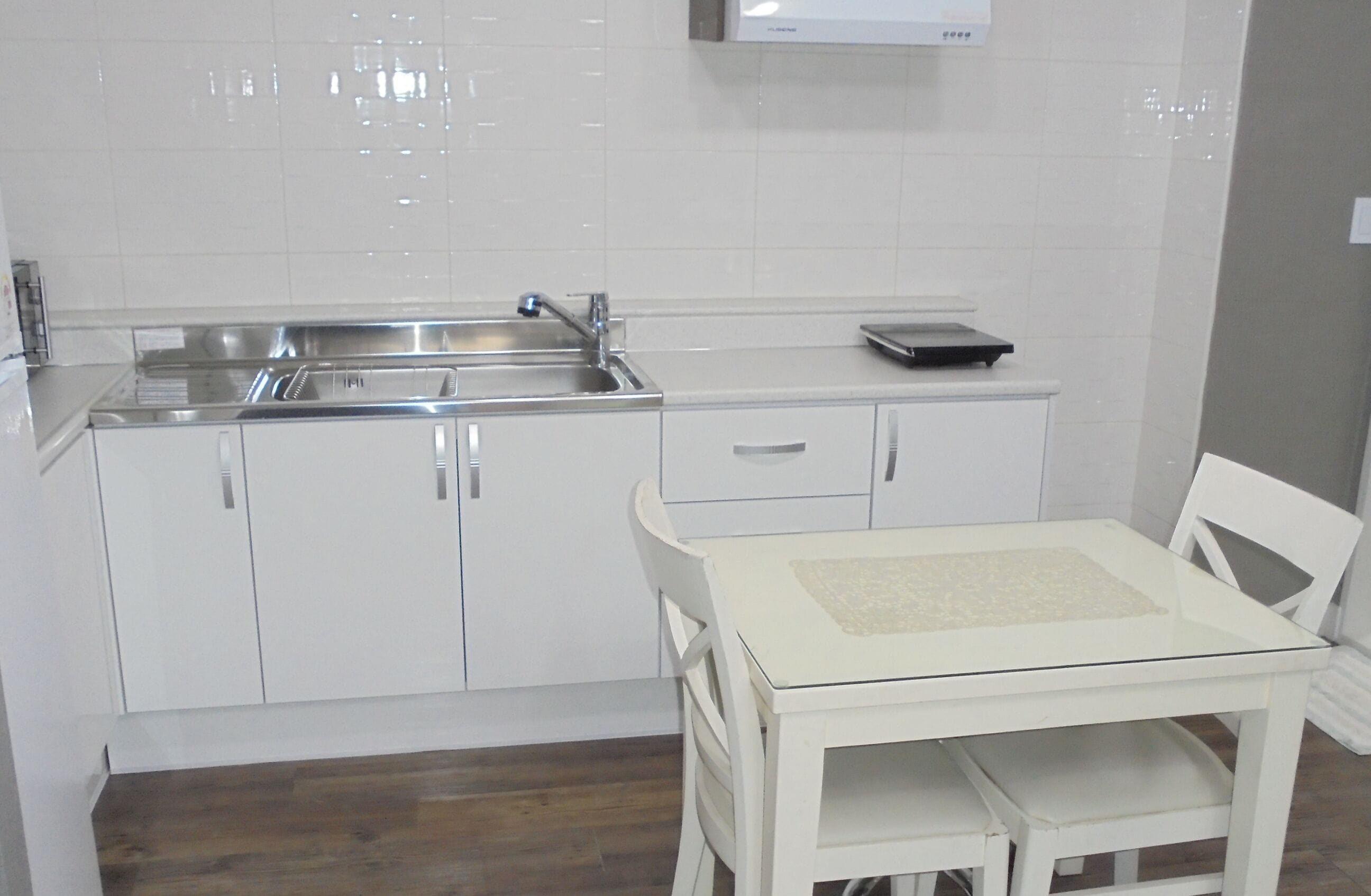 A modern kitchen with white cabinetry, a stainless steel sink, and a small table with chairs.