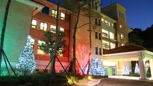A hotel with multiple floors, a covered entrance, and Christmas trees adorned with lights. - Pinehills Hotel (Suncheon)