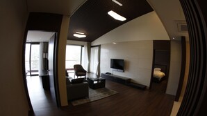 A modern living room with a sofa, coffee table, and TV. There is a balcony visible through the window. - Pinehills Hotel (Suncheon)