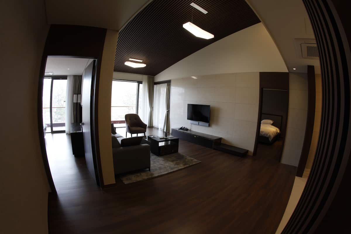 A modern living room with a sofa, coffee table, and TV. There is a balcony visible through the window.