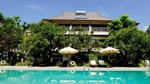 A swimming pool with lounge chairs and umbrellas, surrounded by lush greenery and a large building with a balcony. - Chiangmai Highlands Golf and Spa Resort (Mae On)