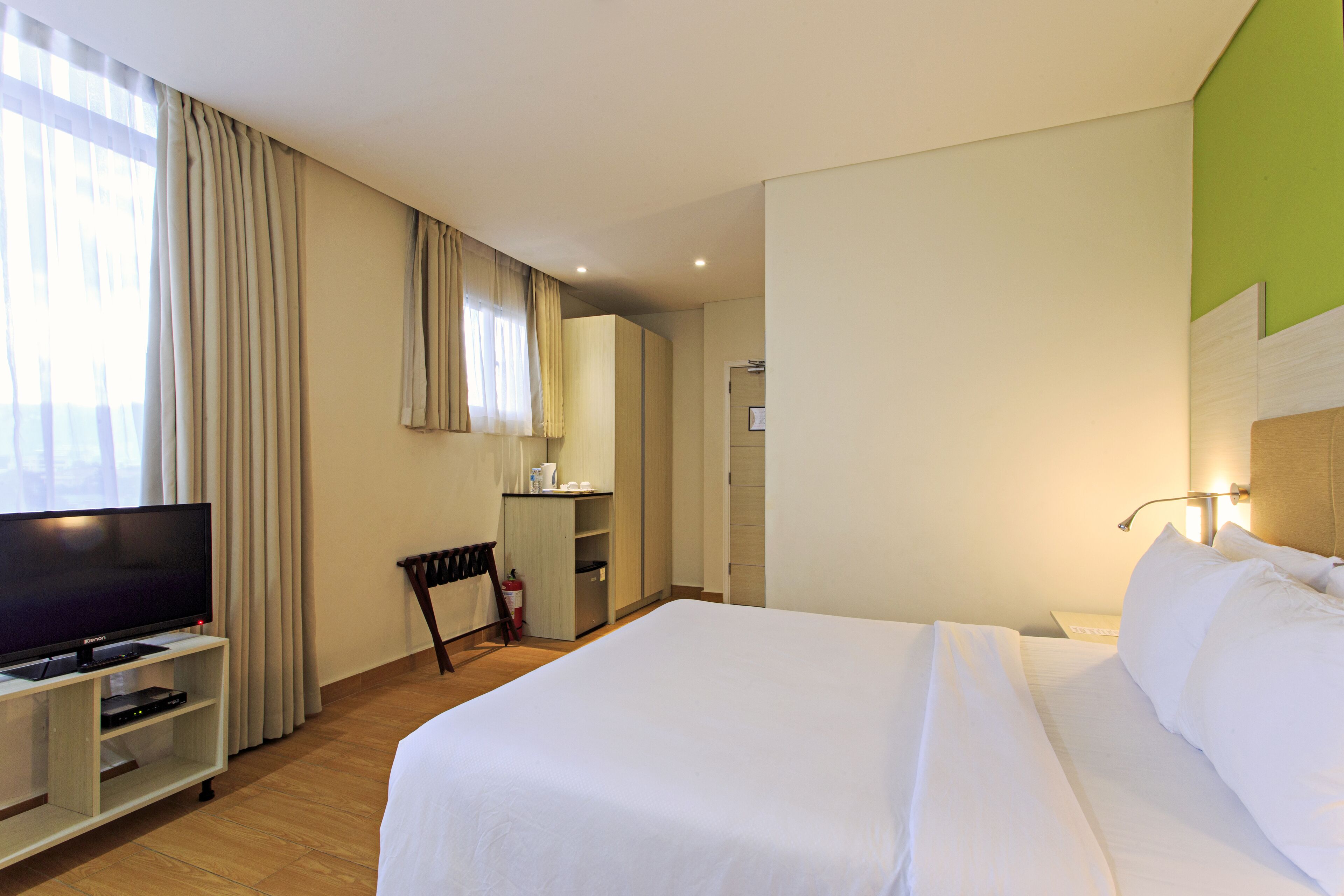 A hotel room with a large bed, a television on a stand, a desk with a chair, and a wardrobe.