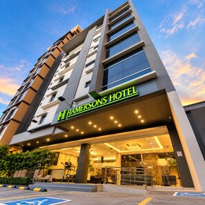 Moderni hotellirakennus, jossa on huomiota herättävä sisäänkäynti, selkeästi näkyvä kyltti ja taustalla avoin, kirkas taivas.
