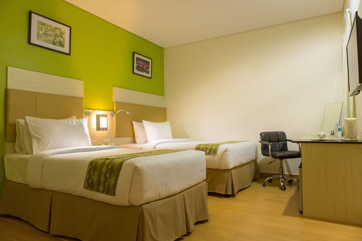A hotel room with two beds, a desk, and a chair.