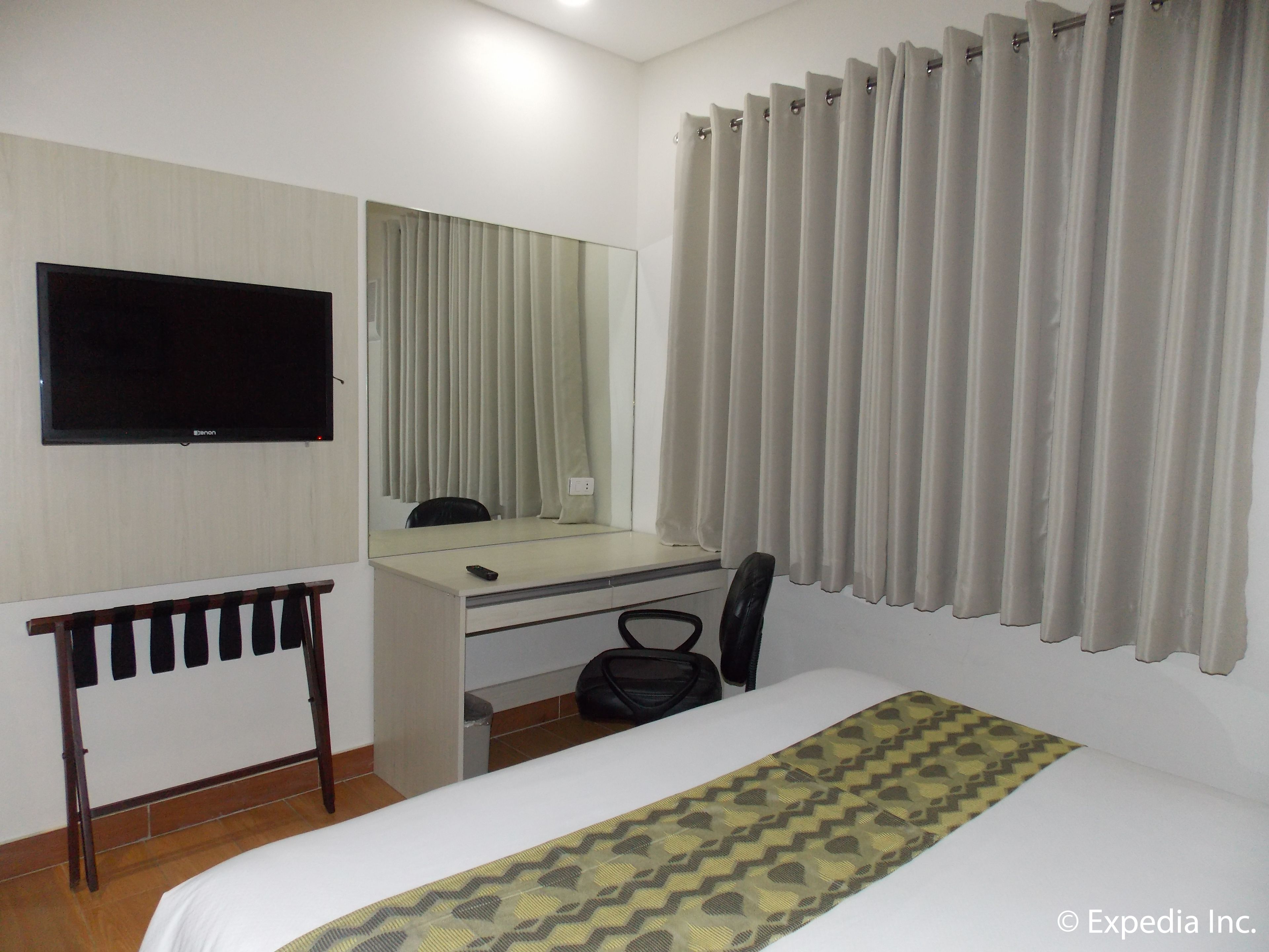 A hotel room with a bed, a desk with a chair, a television, and a window with curtains.