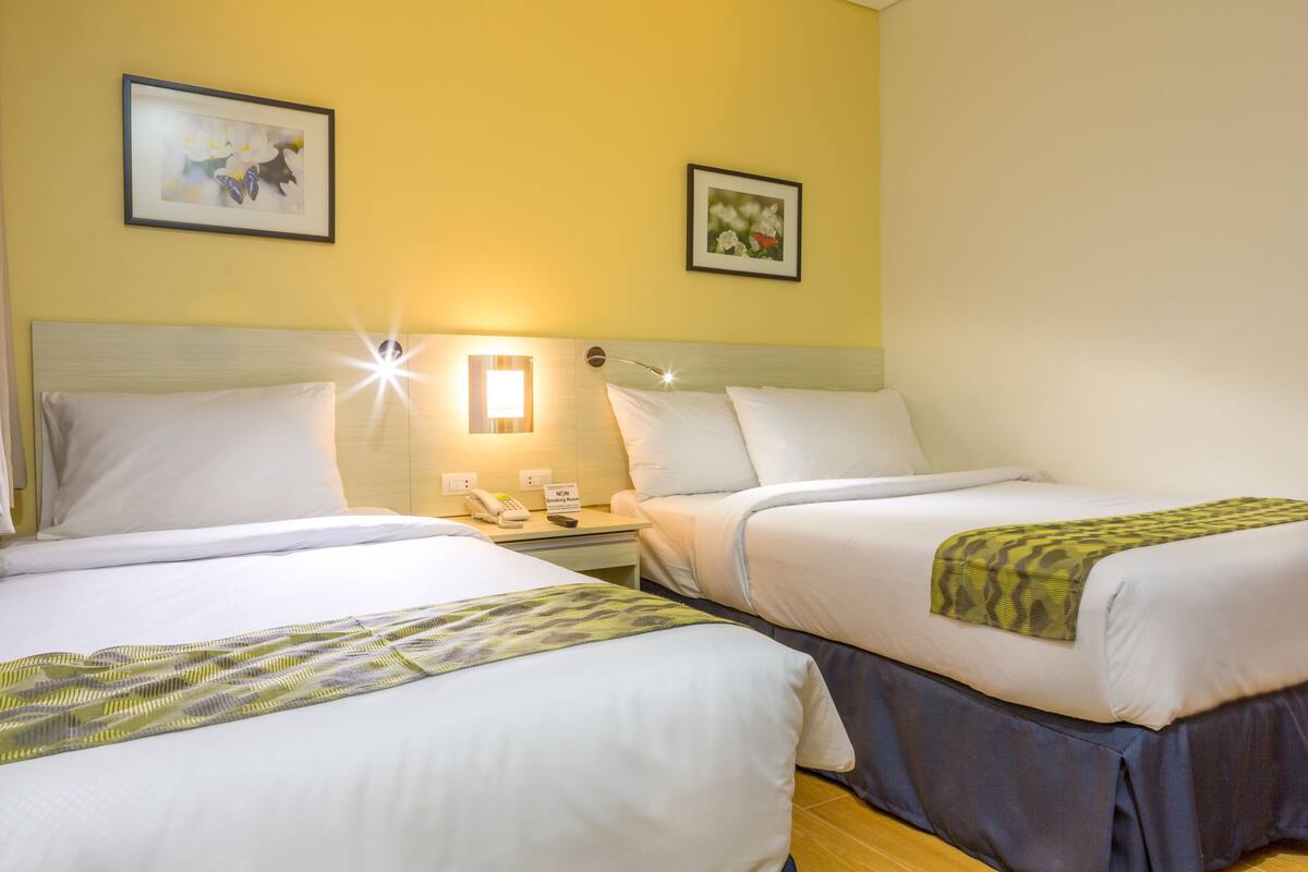 A hotel room with two beds, a nightstand with a phone and lamp, and two framed pictures on the wall.