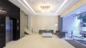 Un vestíbulo moderno con candelabro, escalera, mostrador de recepción y zona de estar.