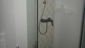 Una ducha con cerramiento de vidrio, cabezal de ducha de mano y llave en la pared.