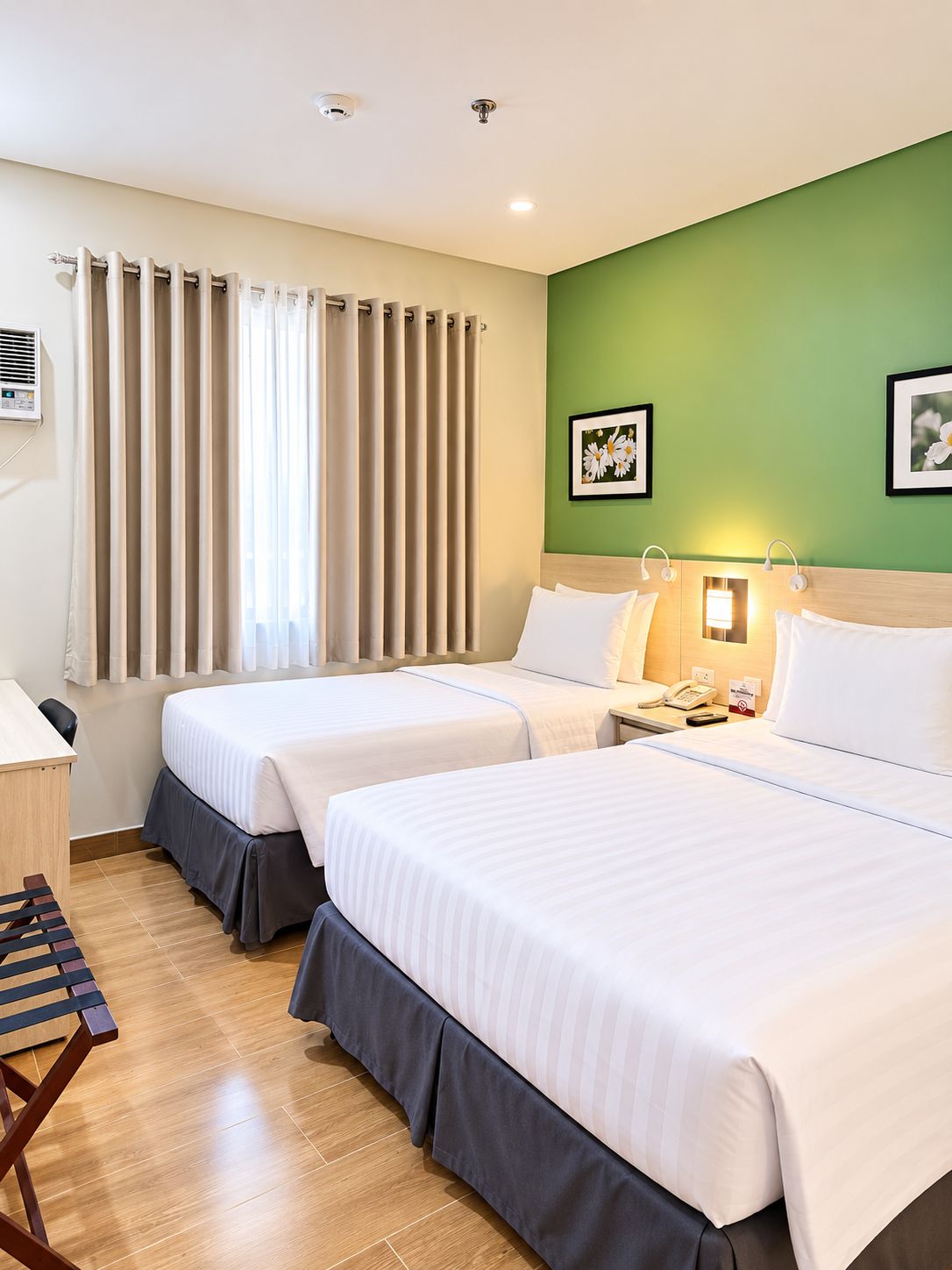 Habitación de hotel con dos camas, un escritorio, una silla, un teléfono y un equipo de aire acondicionado instalado en la pared.