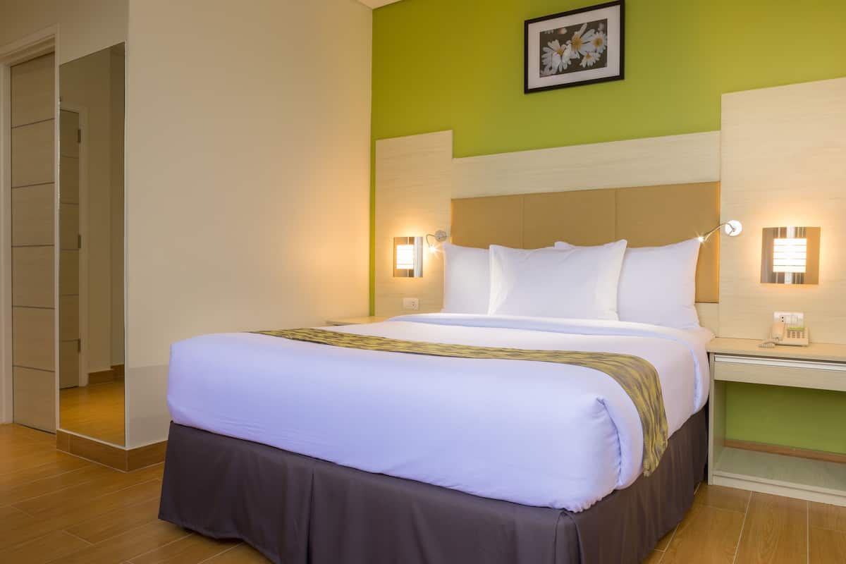 A hotel room with a large bed, bedside lamps, a nightstand, and a framed picture on the wall.