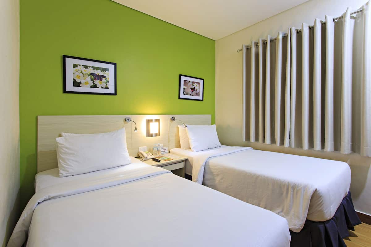 A hotel room with two beds, a nightstand, a telephone, and two framed pictures on the wall.