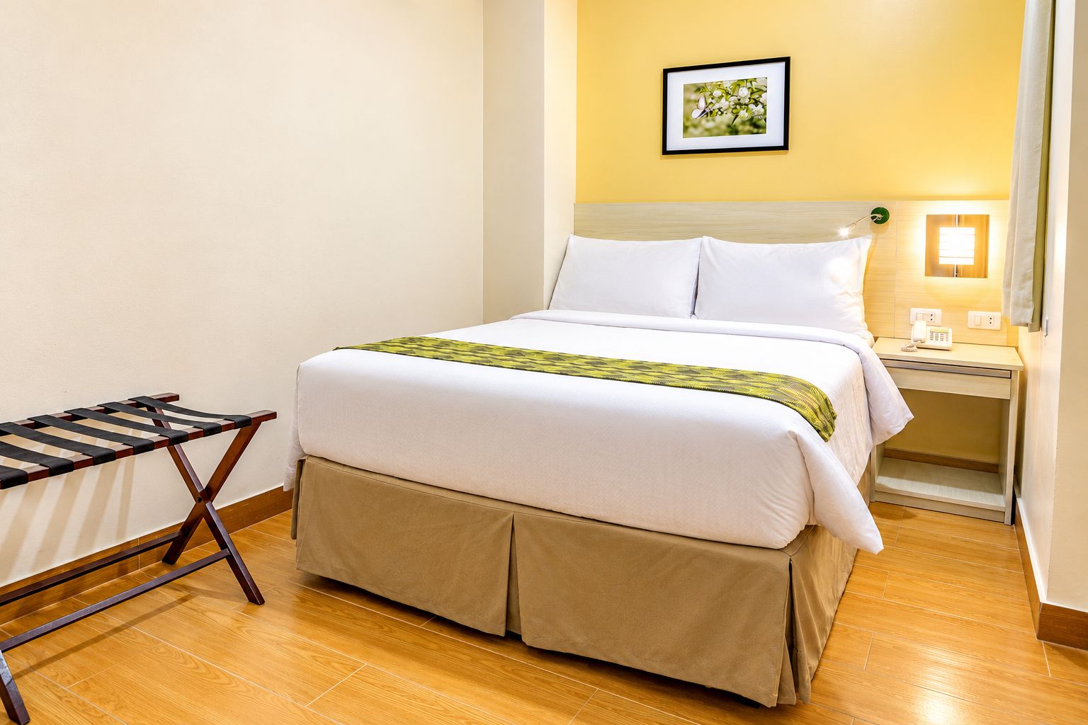 Una habitación de hotel con una cama, una mesita de noche, una lámpara y un cuadro en la pared.