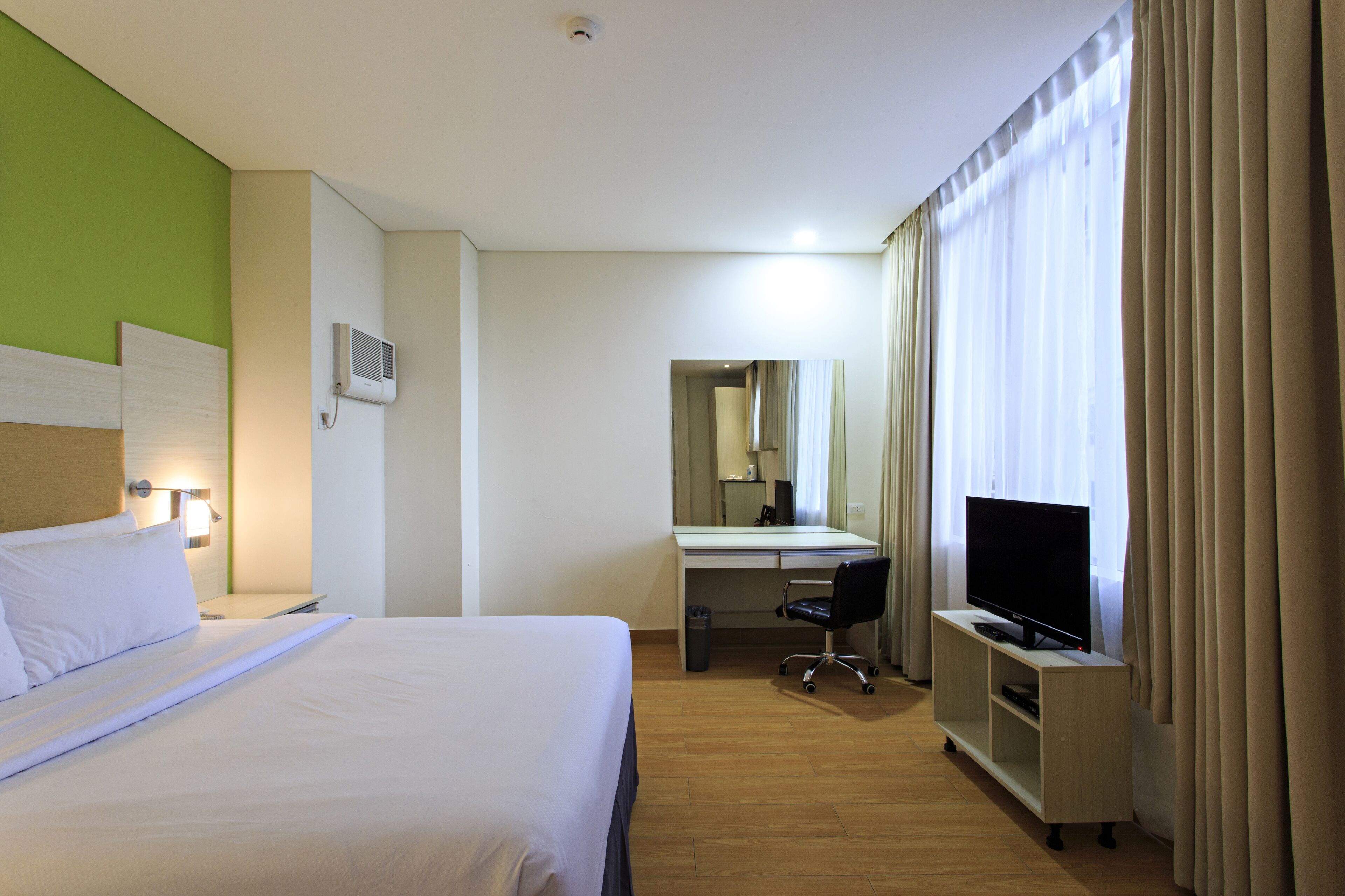 A hotel room with a bed, a desk with a chair, a television, and a mirror.