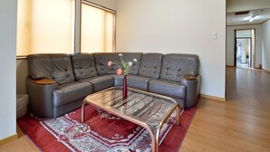Ein Wohnzimmer mit einem Ecksofa, einem Glastisch und einem roten Teppich mit Muster.