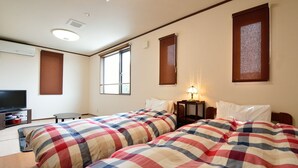 Ein Hotelzimmer mit zwei Betten, einem Fernseher, einem Schreibtisch und einem Fenster.
