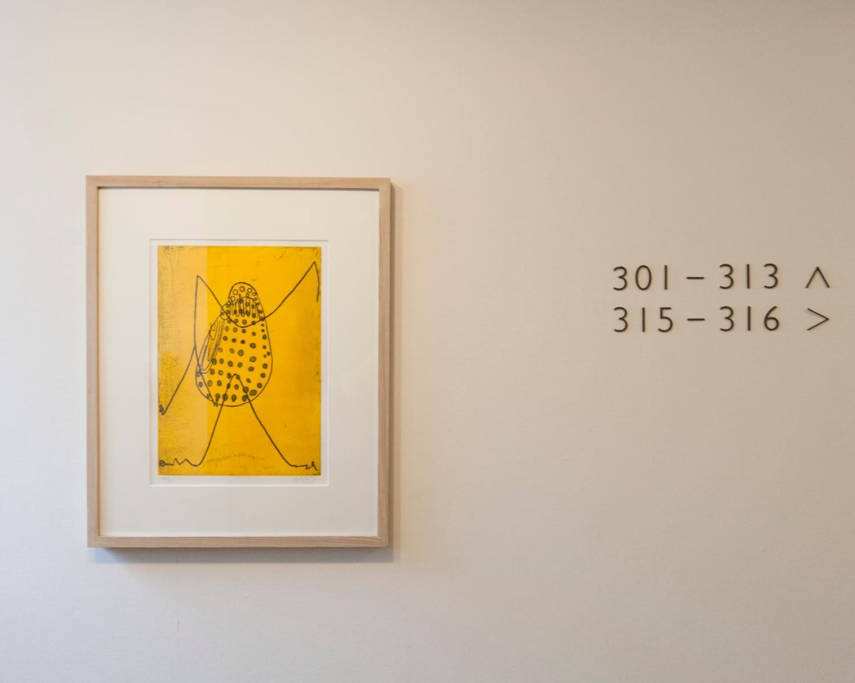A framed artwork with abstract designs on a yellow background, accompanied by text on the wall.