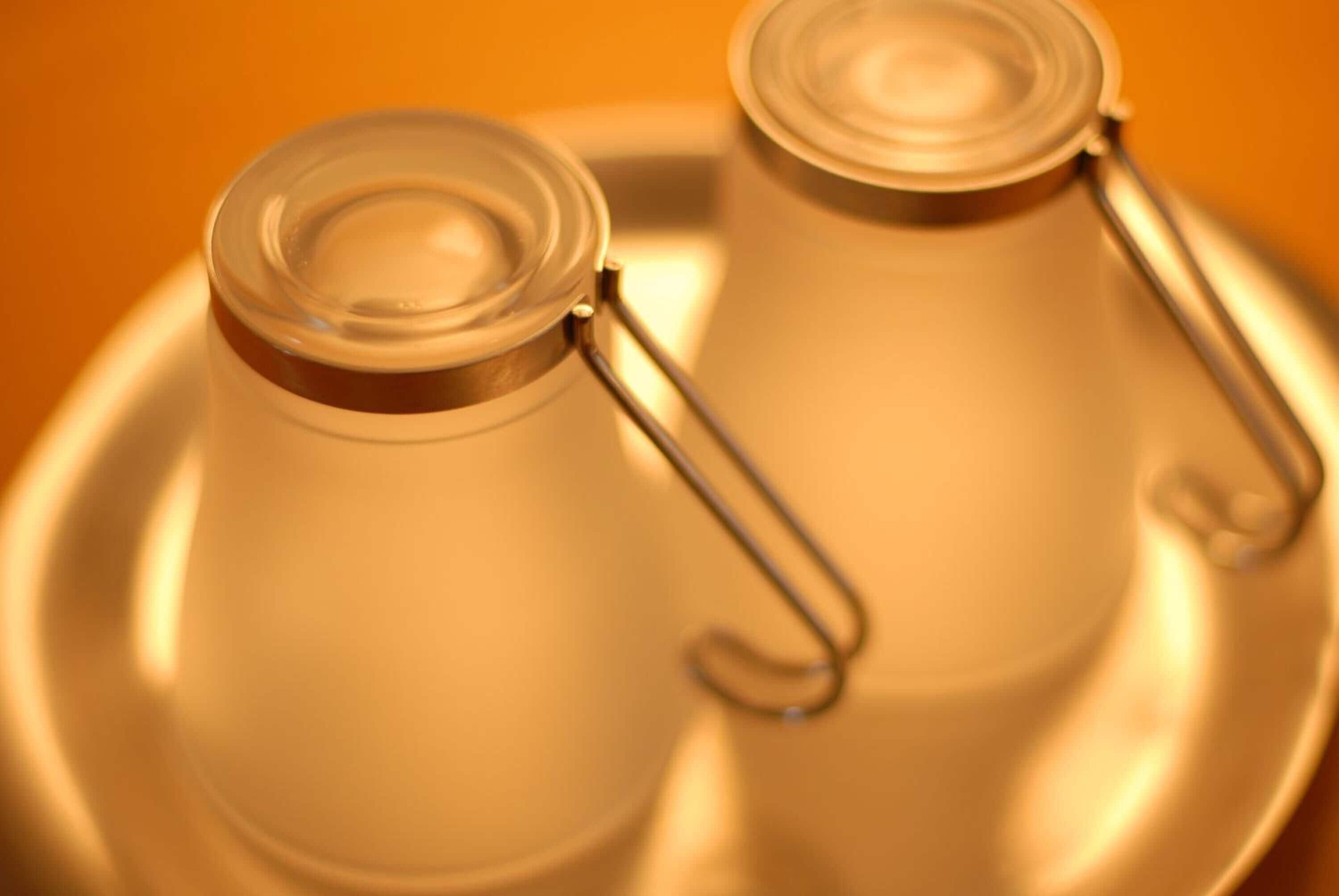 Two glass jars with metal clasps on a reflective surface.