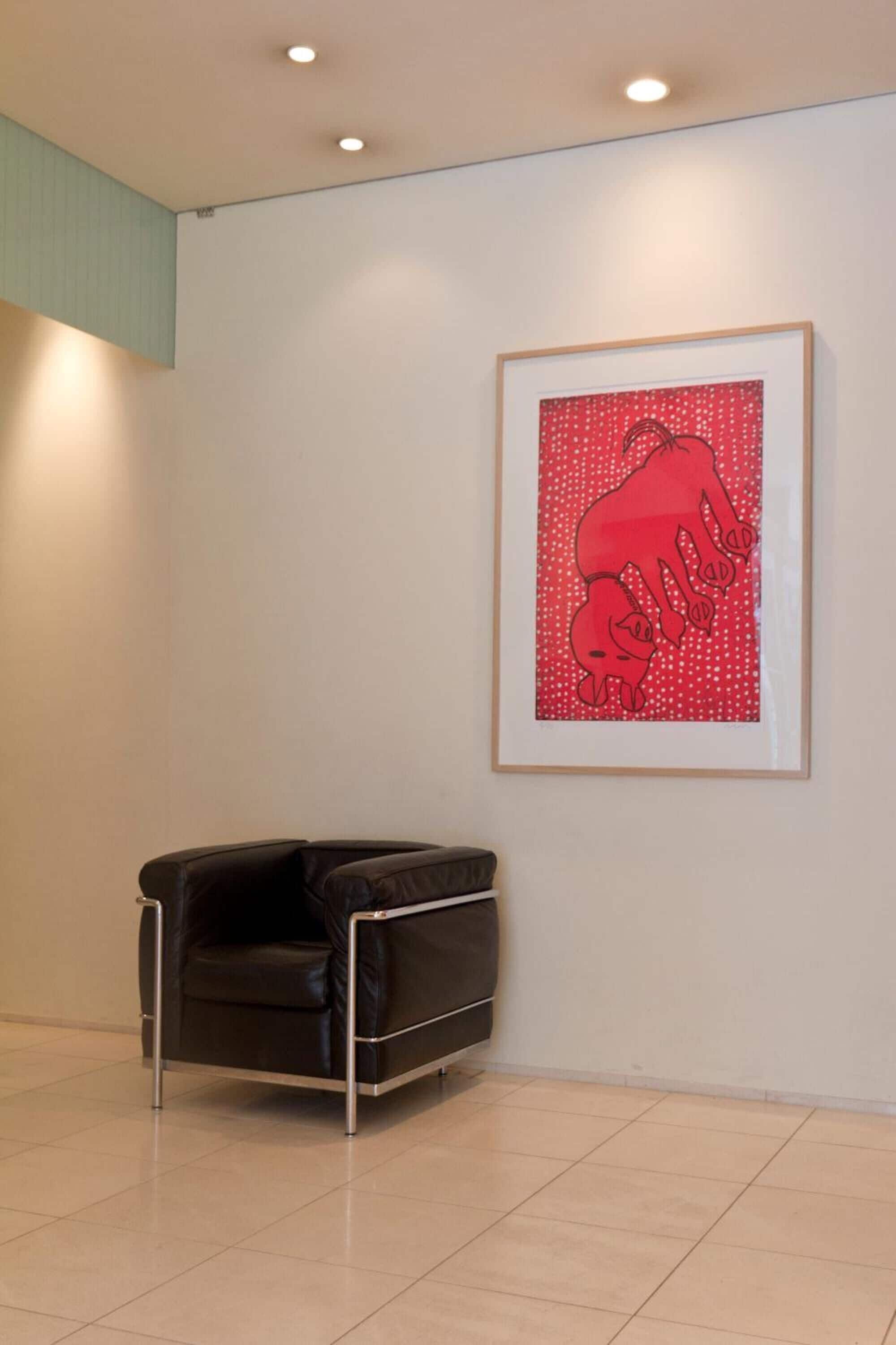 A modern interior with a framed artwork of a red bull on a white wall, a black leather chair, and a tiled floor.