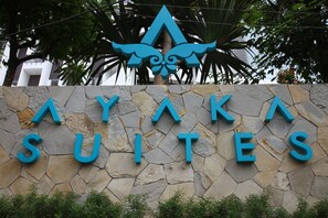 A stone wall with the text "AYAKAS SUITES" and a decorative emblem above it. - Ayaka Suites (Jakarta)