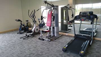 Un gimnasio con diversos equipos de ejercicio, incluyendo una cinta de correr, una elíptica y máquinas de pesas.