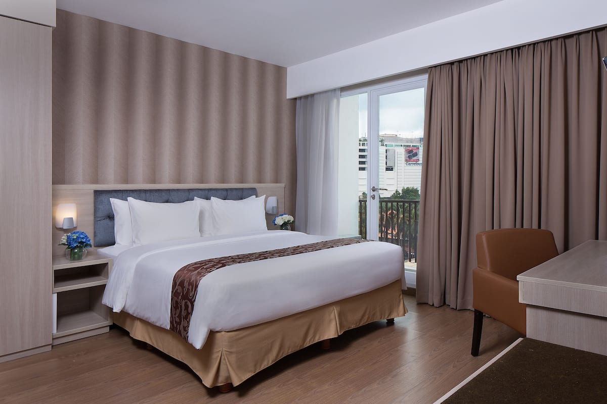 Ein Hotelzimmer mit einem großen Bett, einem Schreibtisch und Blick auf die Stadt durch das Fenster.