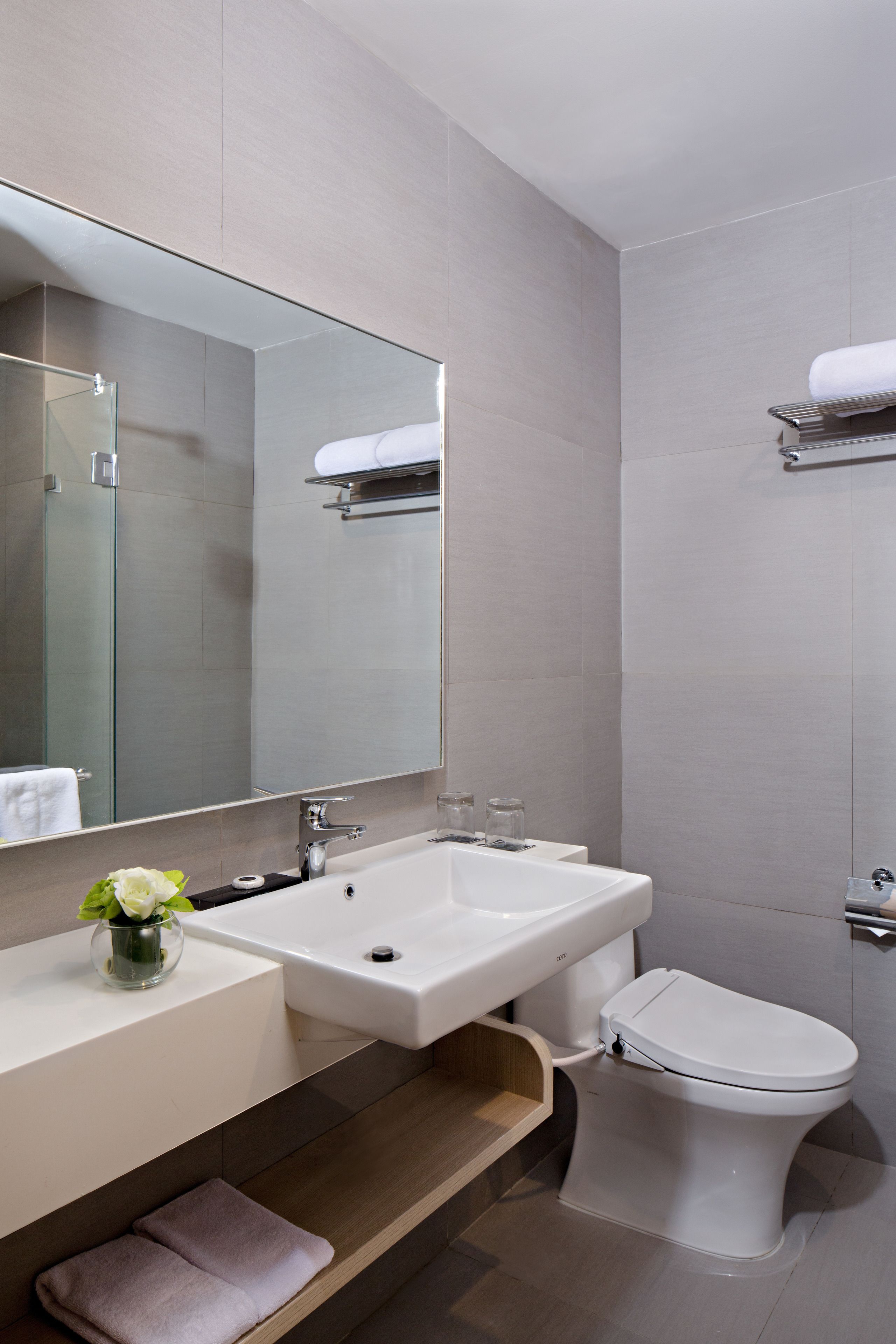 A modern bathroom with a large mirror, white sink, and toilet.