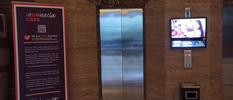An elevator with a digital display and a signboard about Indonesia care standards.