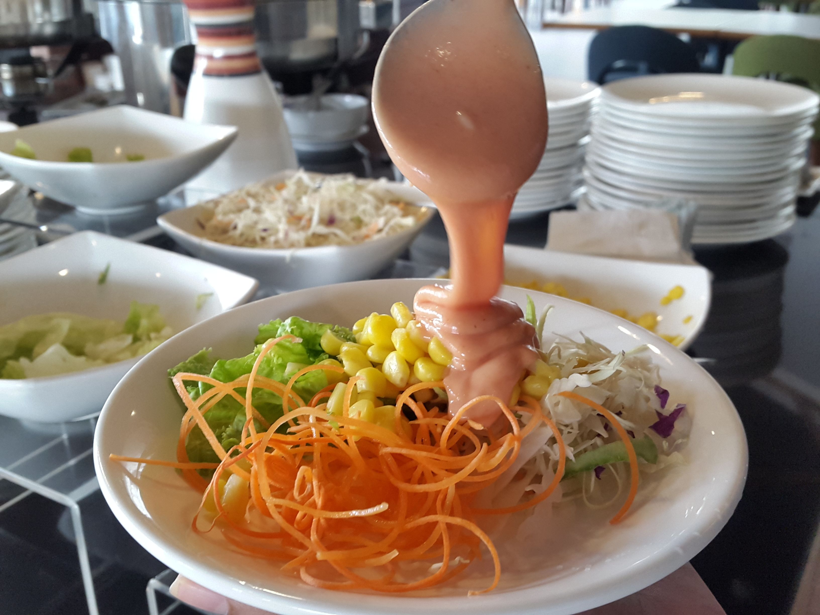 A salad with various vegetables and a dressing being poured over it.