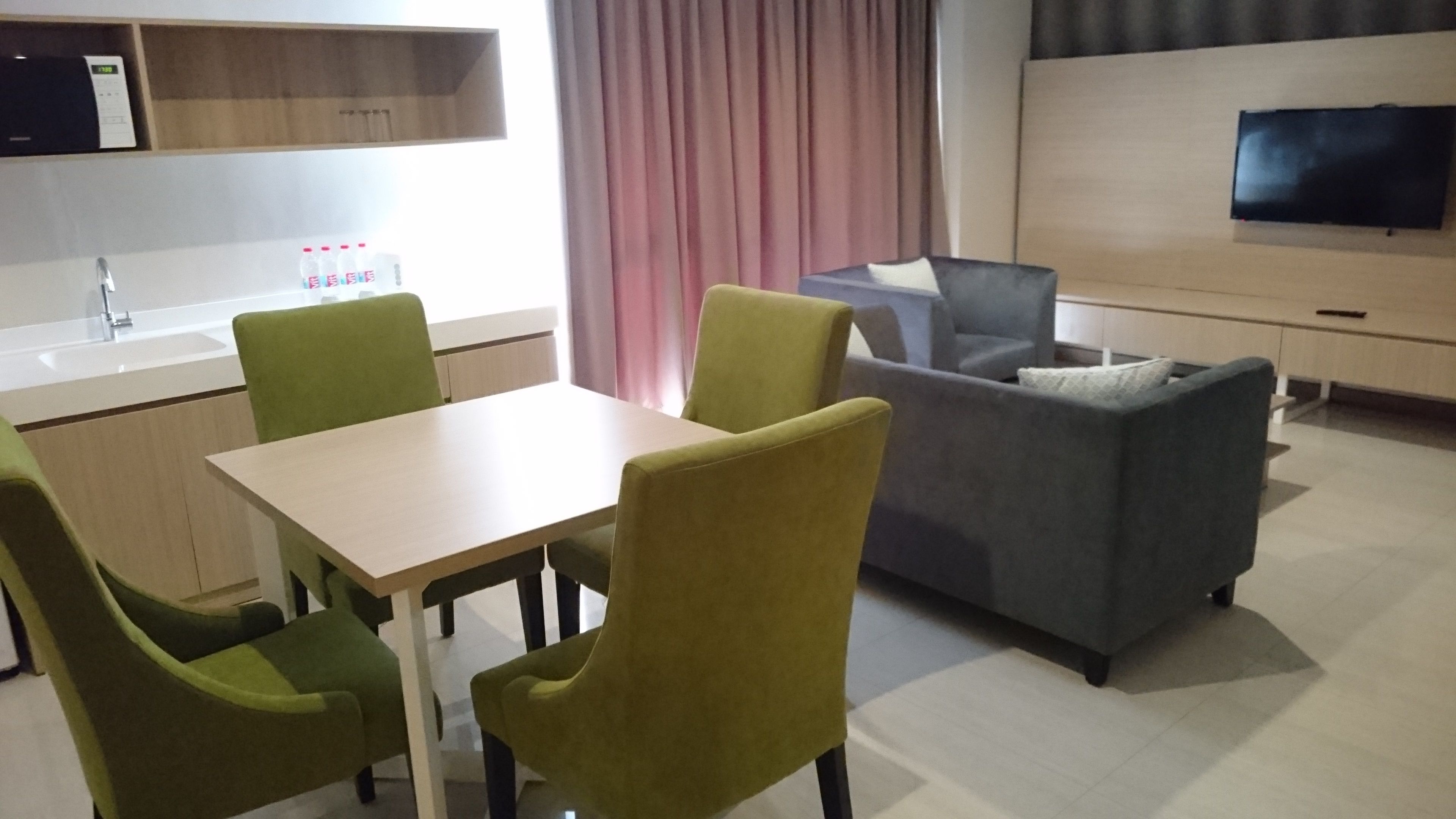 A modern living room with a sofa, two green chairs, a table, and a TV mounted on the wall.