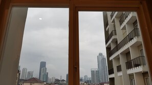 A view through a window of a cityscape with high-rise buildings and a balcony with black railings. - Ayaka Suites (Jakarta)