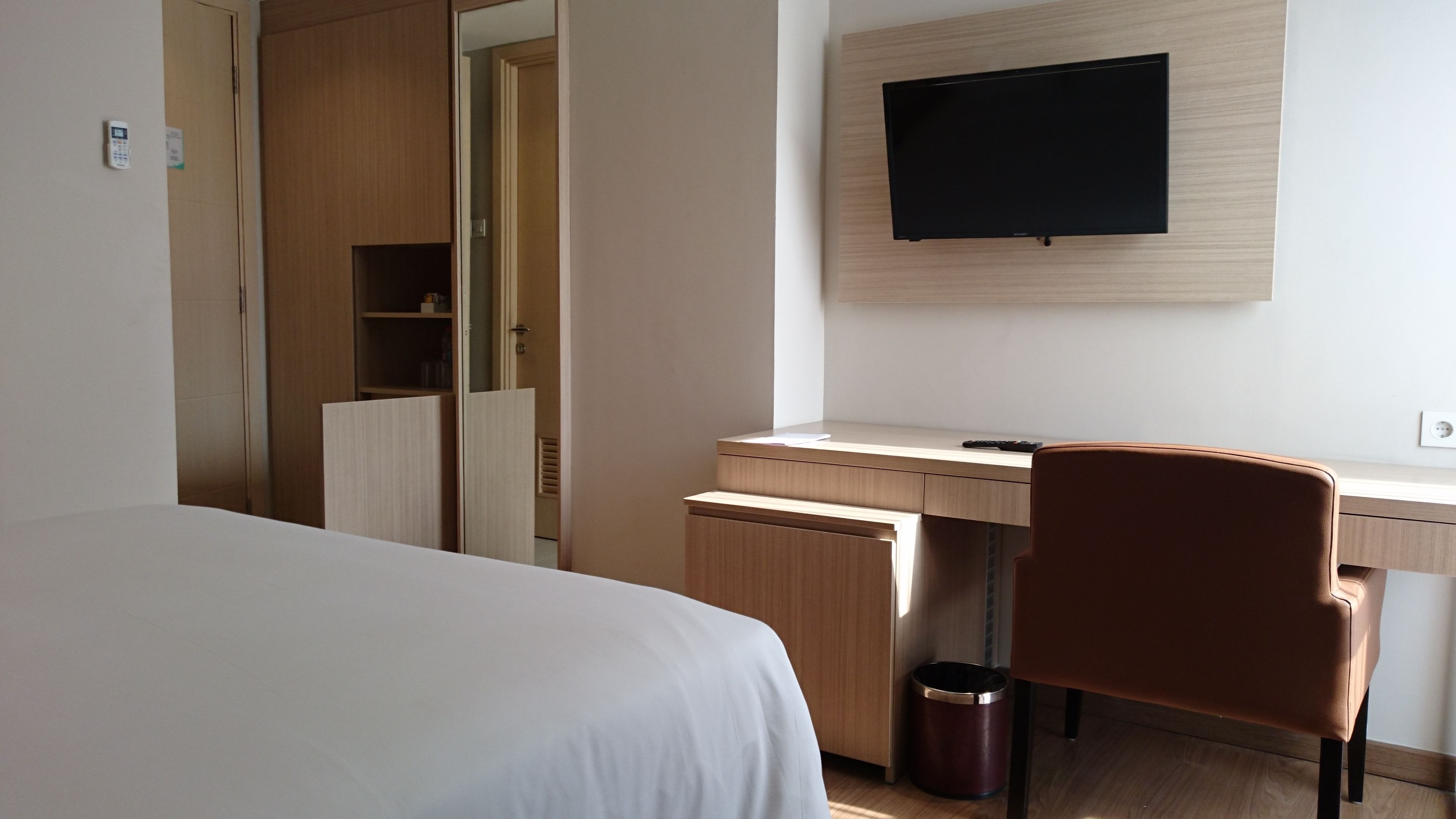 Una habitación de hotel con cama, escritorio, silla, televisor y un cesto de basura.
