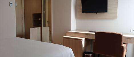 A hotel room with a bed, a desk, a chair, a TV, and a trash bin.