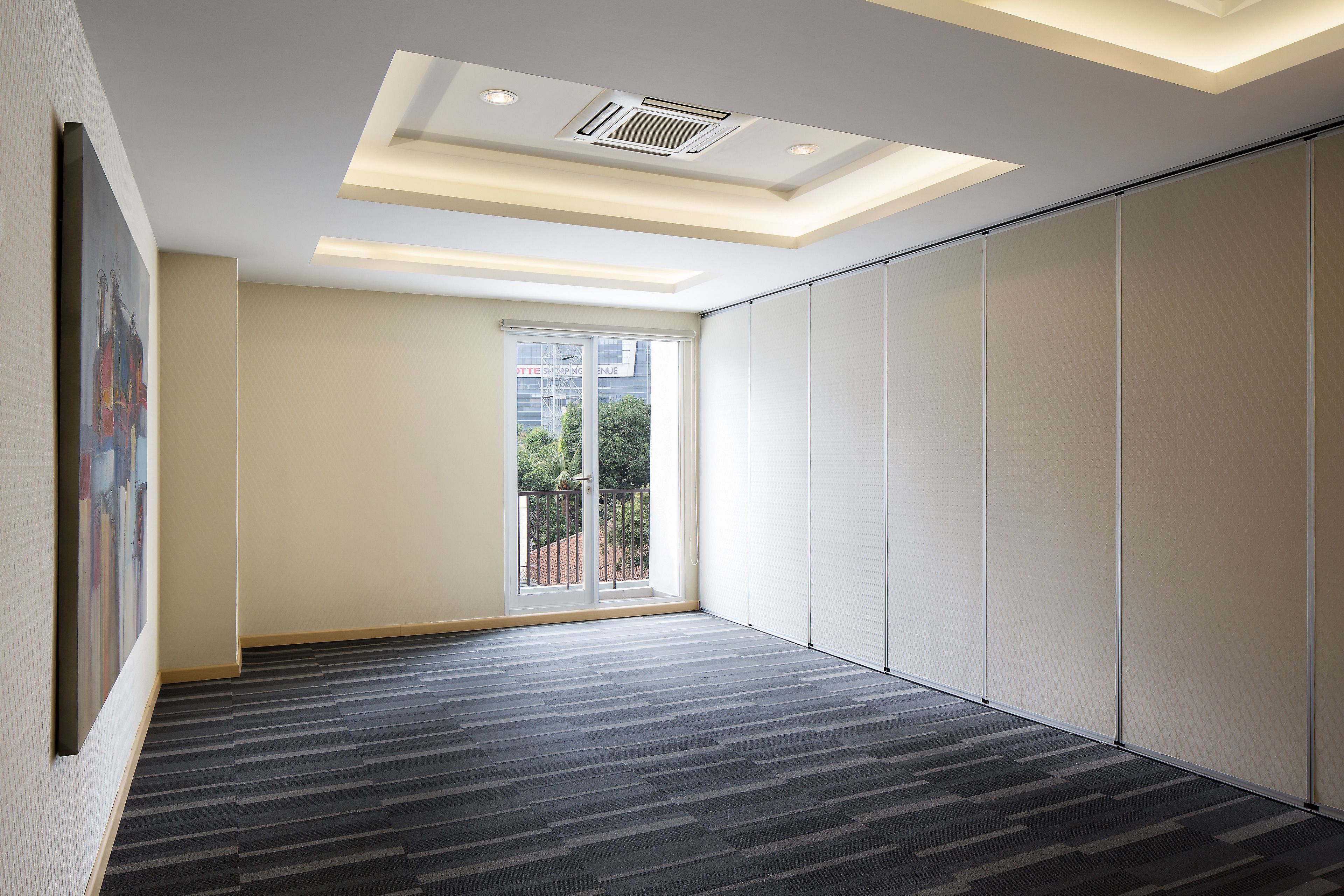 A spacious room with a modern ceiling design, a large sliding door leading to an outdoor area, and a patterned carpet.