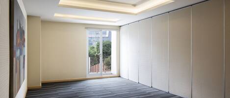 A spacious room with a modern ceiling design, a large sliding door leading to an outdoor area, and a patterned carpet.