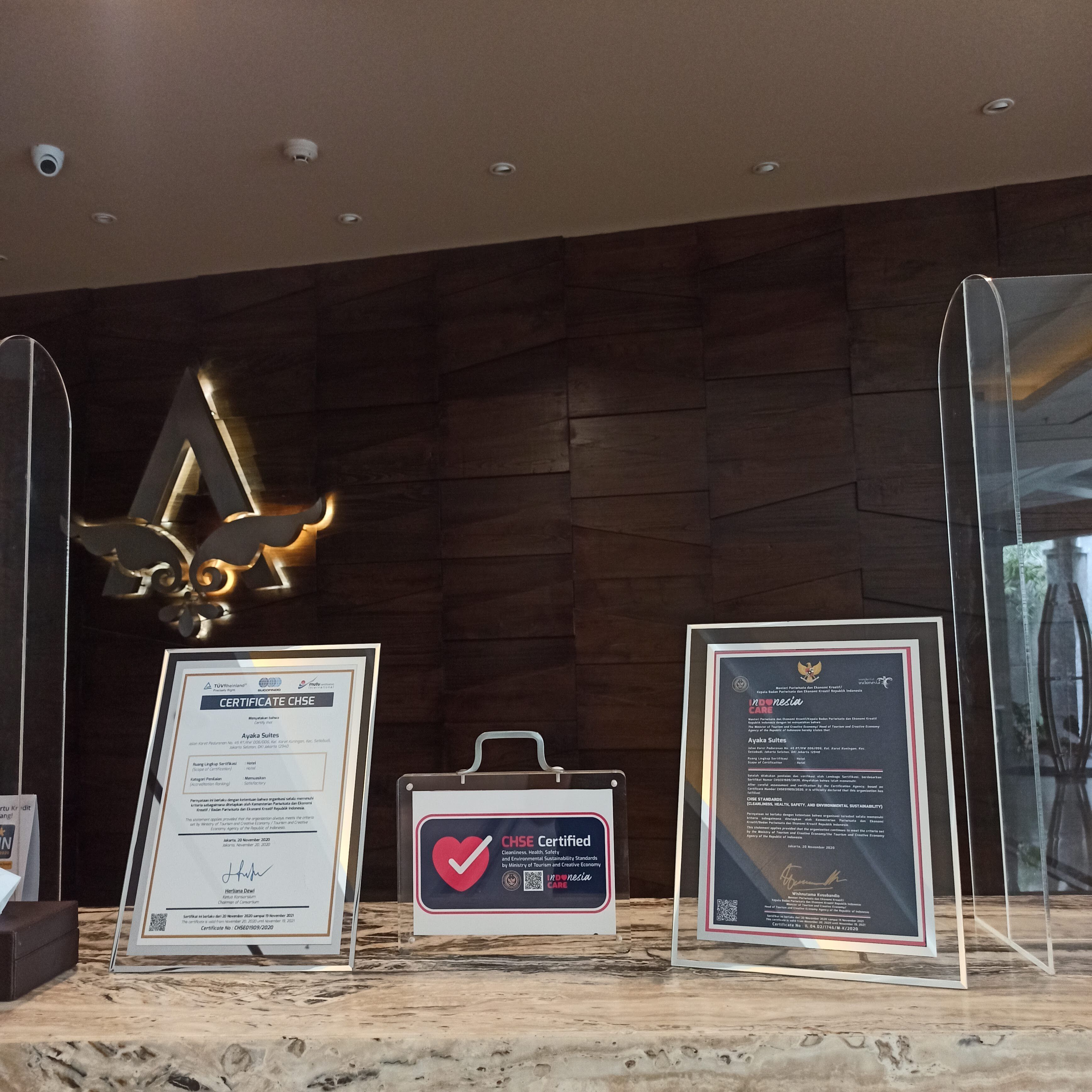 A reception area with a wooden wall, a large illuminated 'A' sign, and three framed documents on a marble counter.